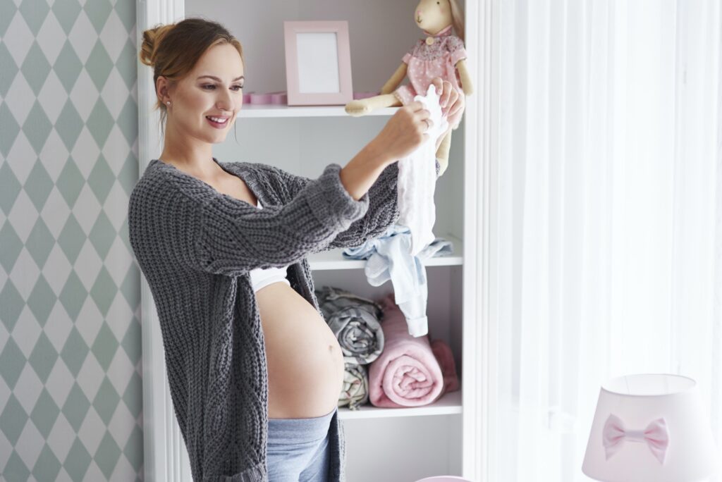 Pregnant woman with baby clothes in baby room
